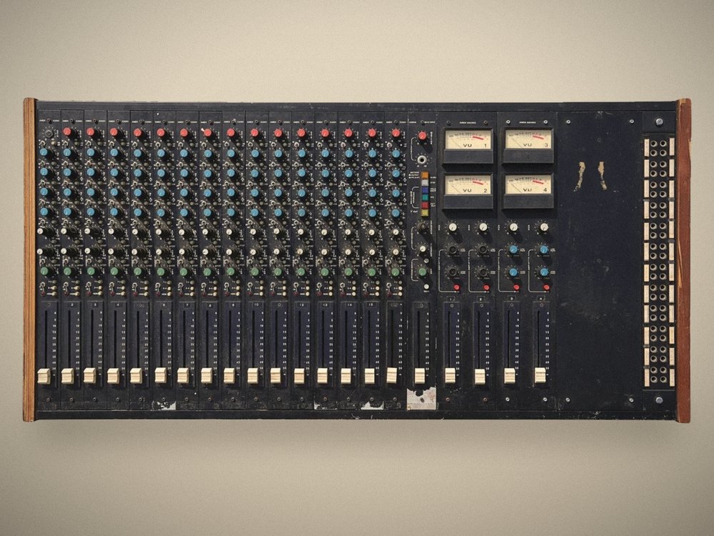 Prince’s AMEK console, front view: 16 channel strips with red, blue and green knobs, four VU meters and a patchbay, in a dark-stained wooden frame